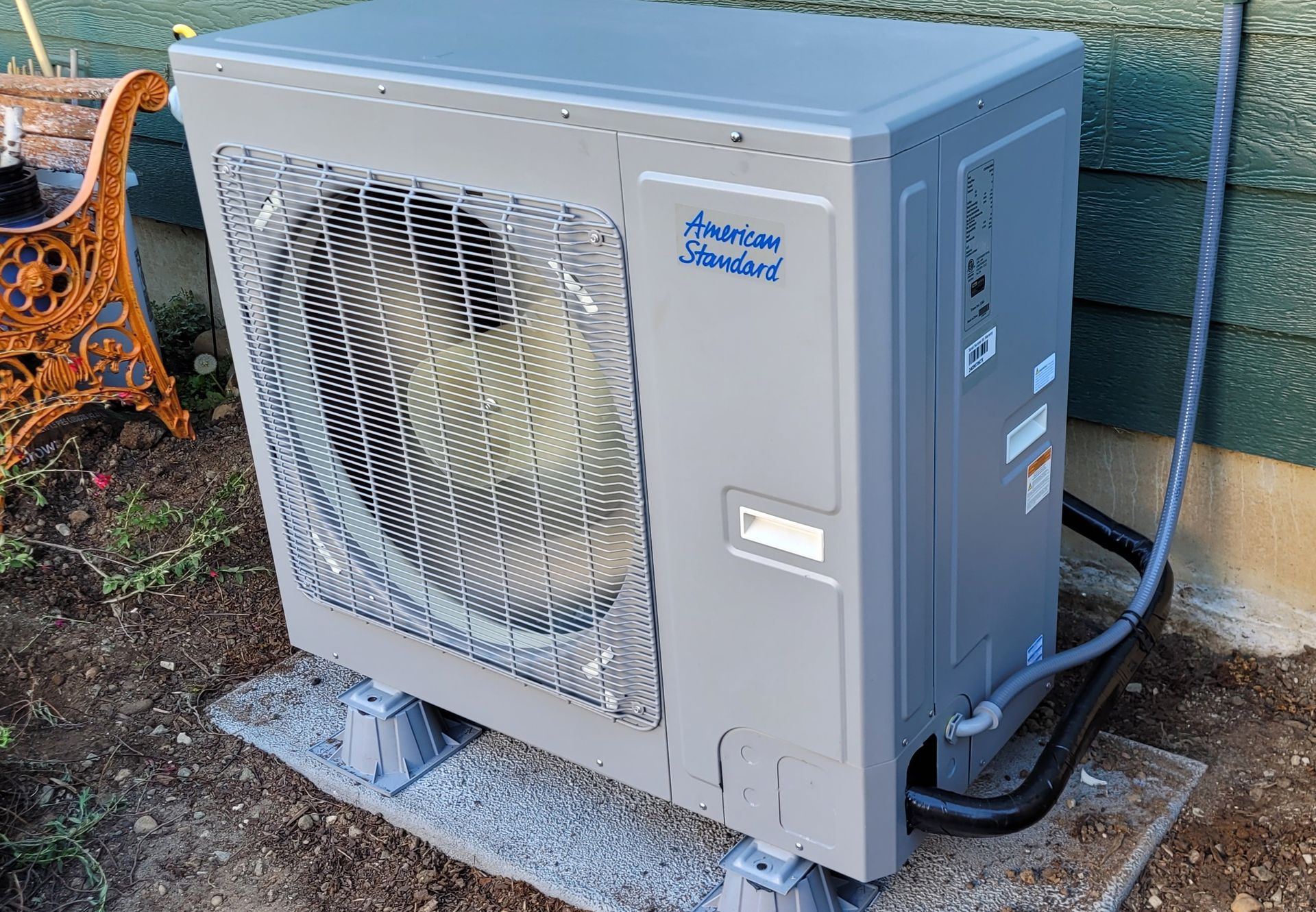 Heavy Metal HVAC LLC - American Standard heat pump unit on a concrete pad by a wall.