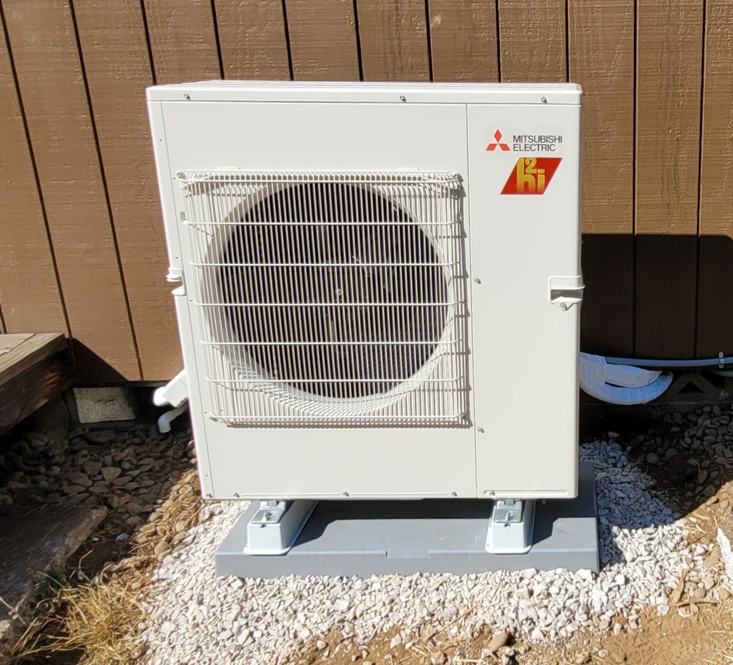 Heavy Metal HVAC llc - Mitsubishi heat pump unit on a gravel bed next to a brown building.