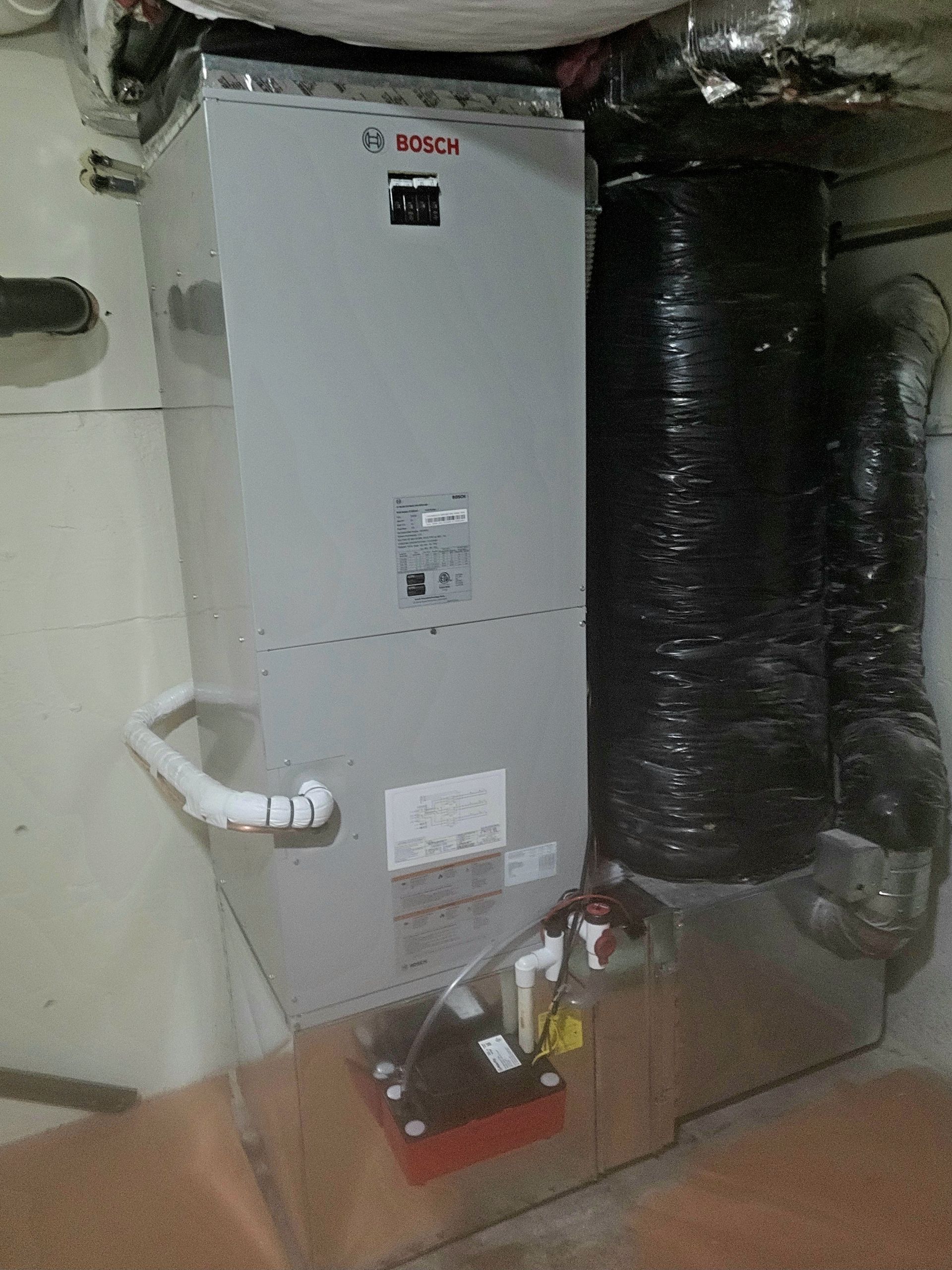 a bosch air conditioner is sitting in a basement next to a duct .