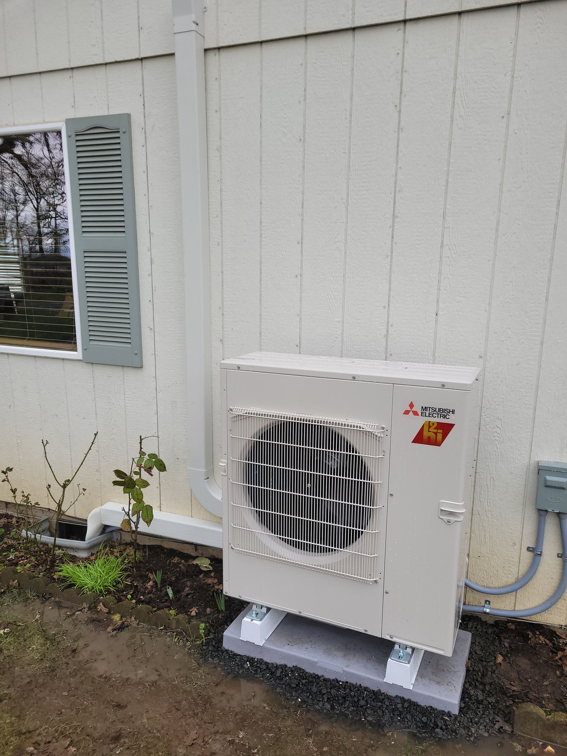a white air conditioner is sitting outside of a house next to a window .