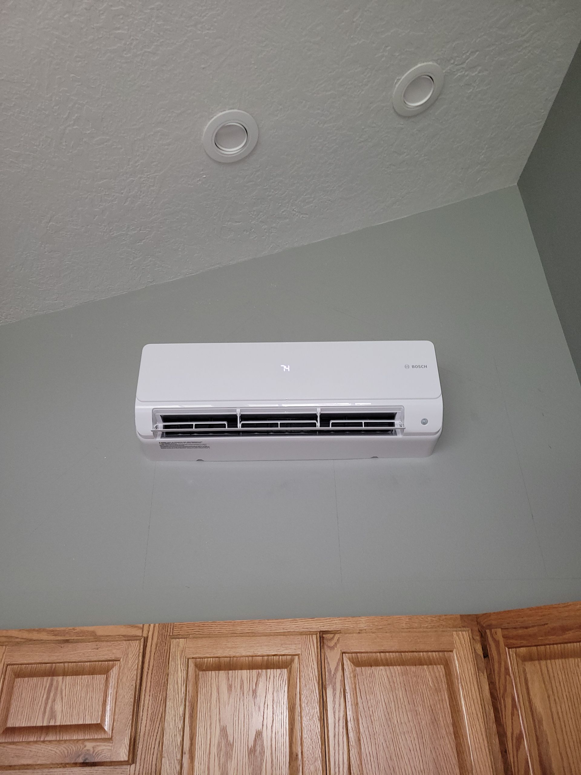 a white air conditioner is hanging from the ceiling in a room with wooden cabinets .