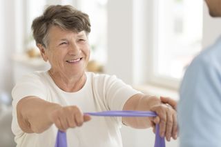 Pphysical Therapy Treatment — Therapist Helping Senior Male To Use Resistance Band in Natick, MA