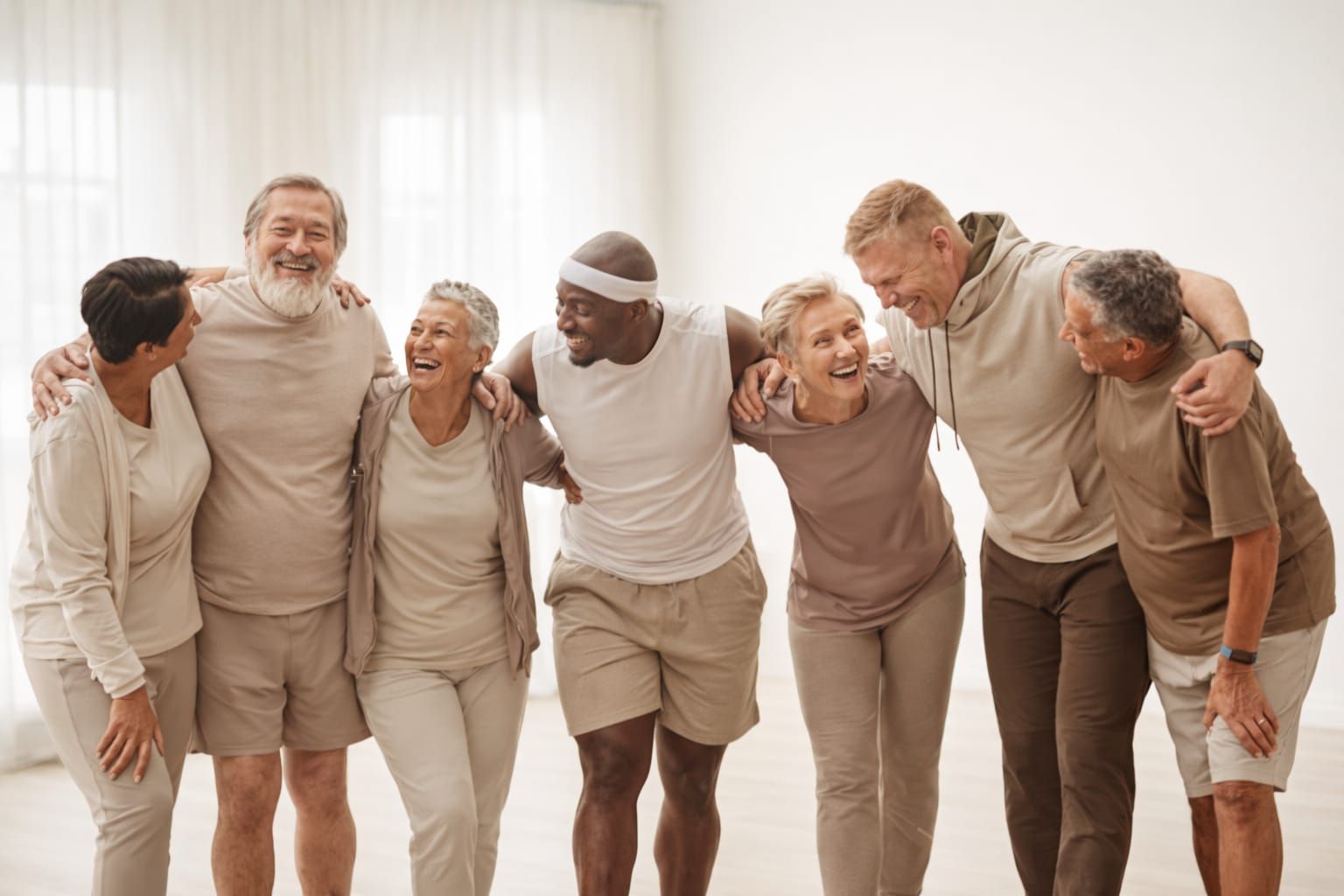 Een groep ouderen in sportkleding, lachend en met de armen om elkaar heen in een lichte ruimte.