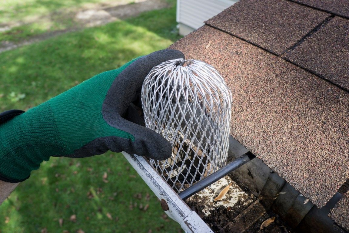 Man using a long pressure washer wand to clean gutters from the ground.