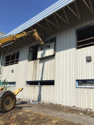 a yellow crane is lifting a window from the side of a building .