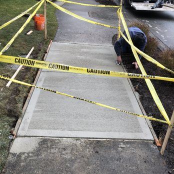 a man is working on a sidewalk surrounded by yellow tape .