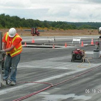 a man wearing a hard hat and safety vest is working on a runway .