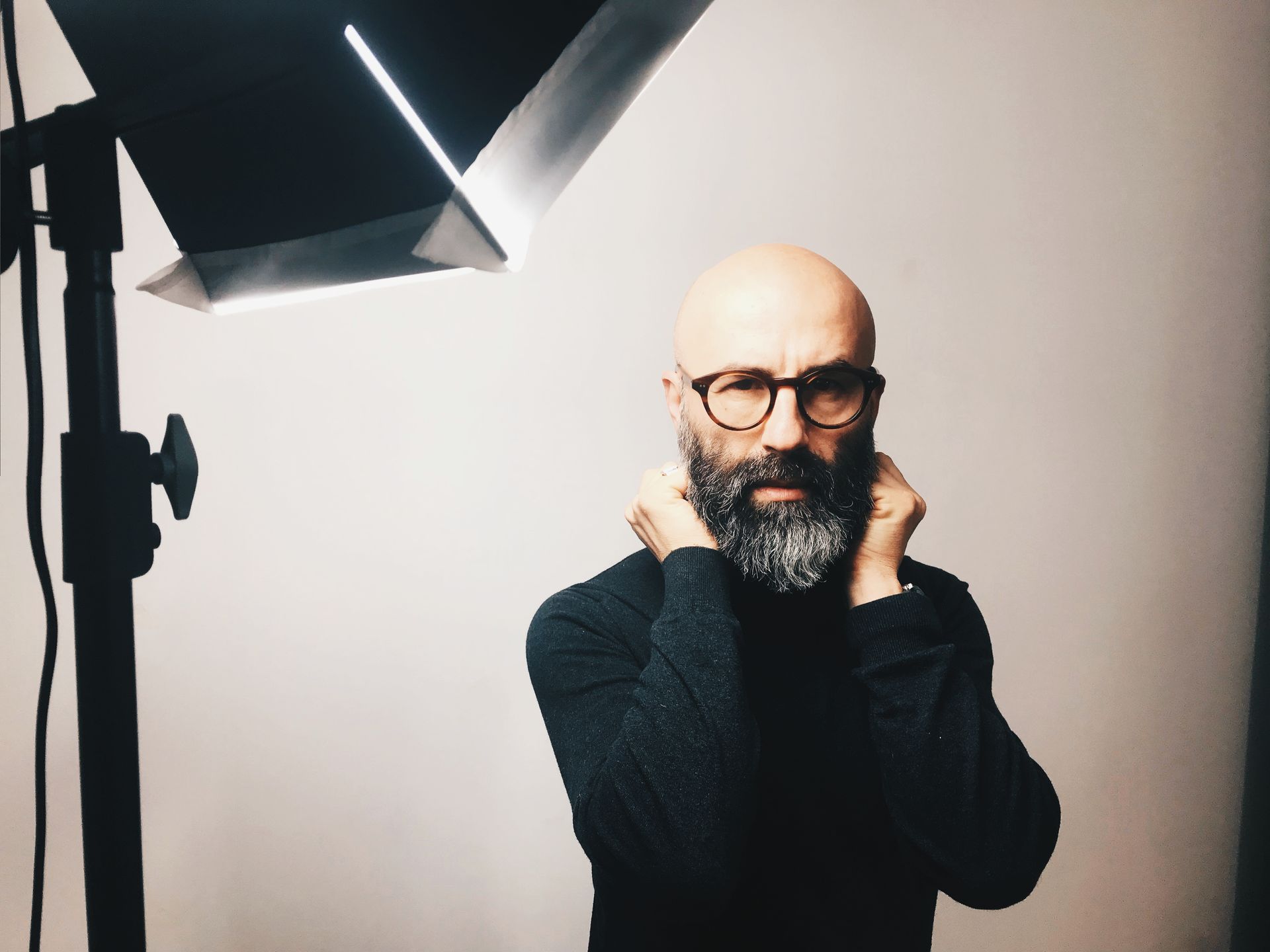 Un hombre calvo con gafas y barba está parado frente a una luz.