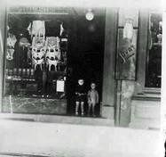 A black and white photo of two children standing in front of a store window.