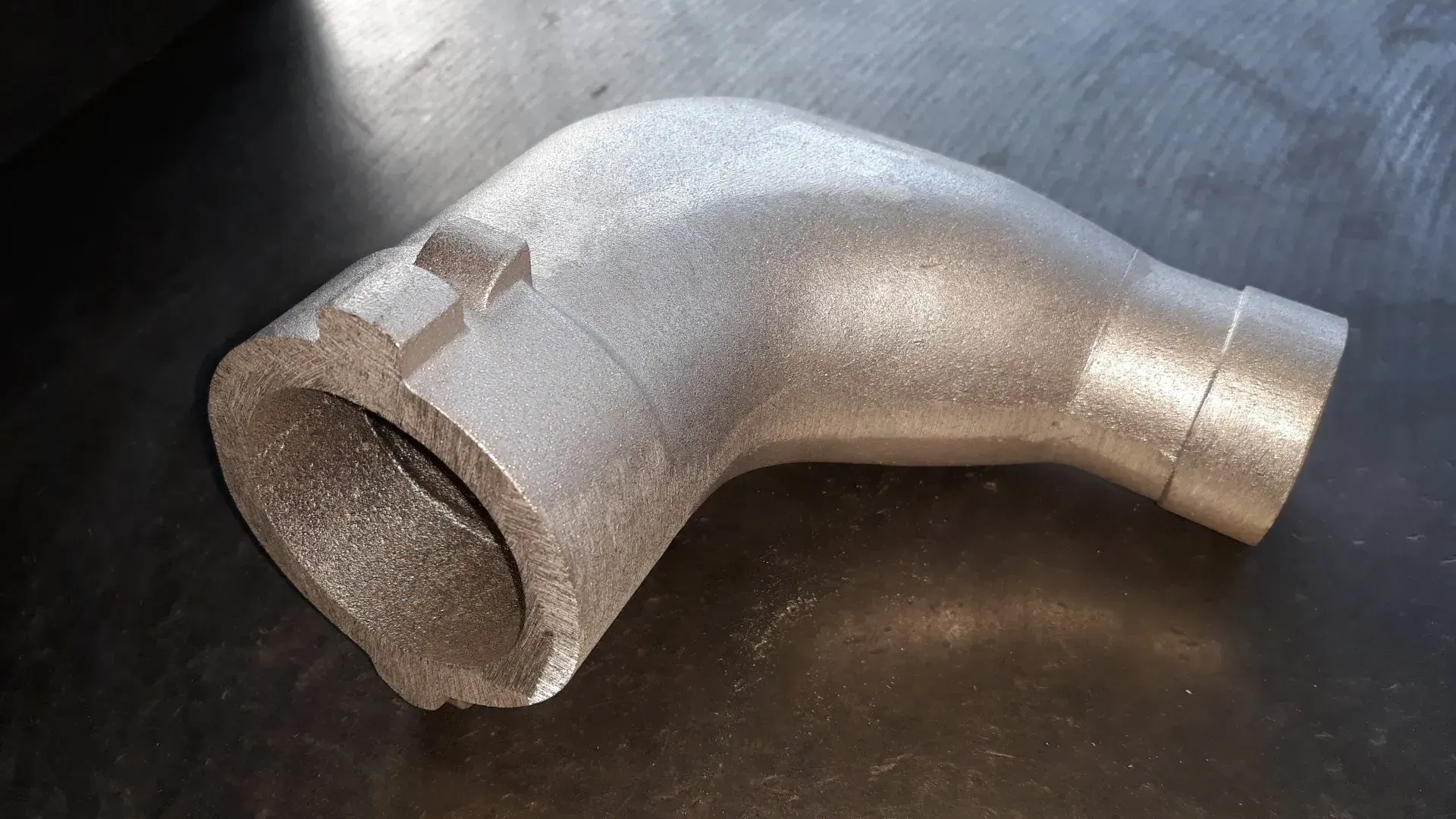 Tubo metallico angolato con superficie strutturata su una superficie metallica riflettente.