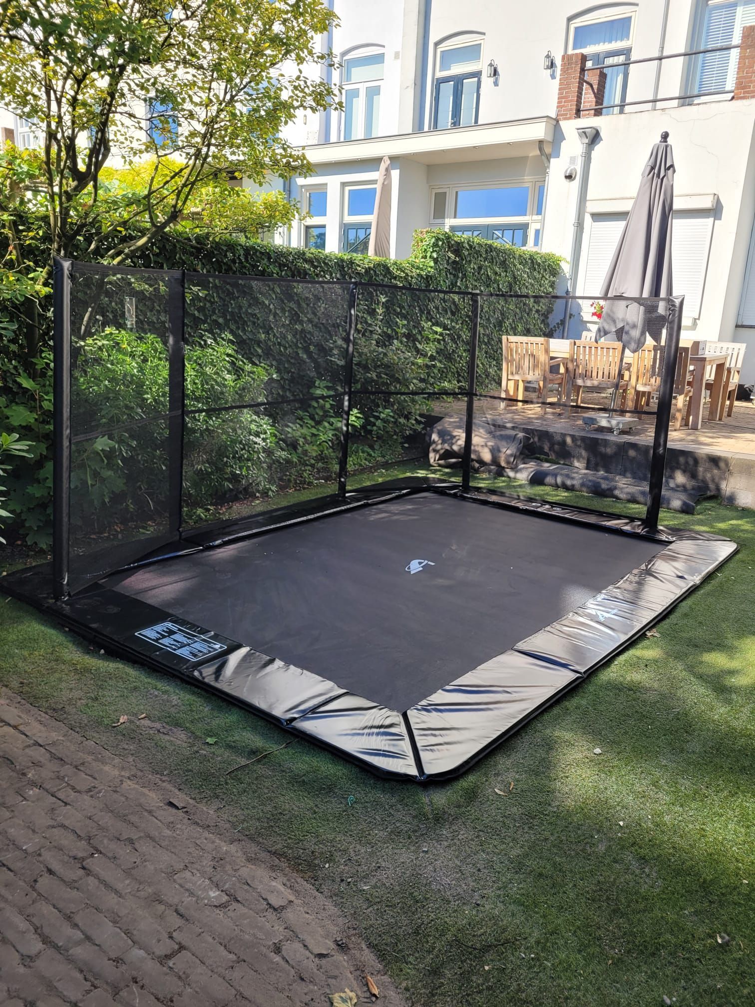 Zwarte rechthoekige trampoline met veiligheidsnet op een grasveld.