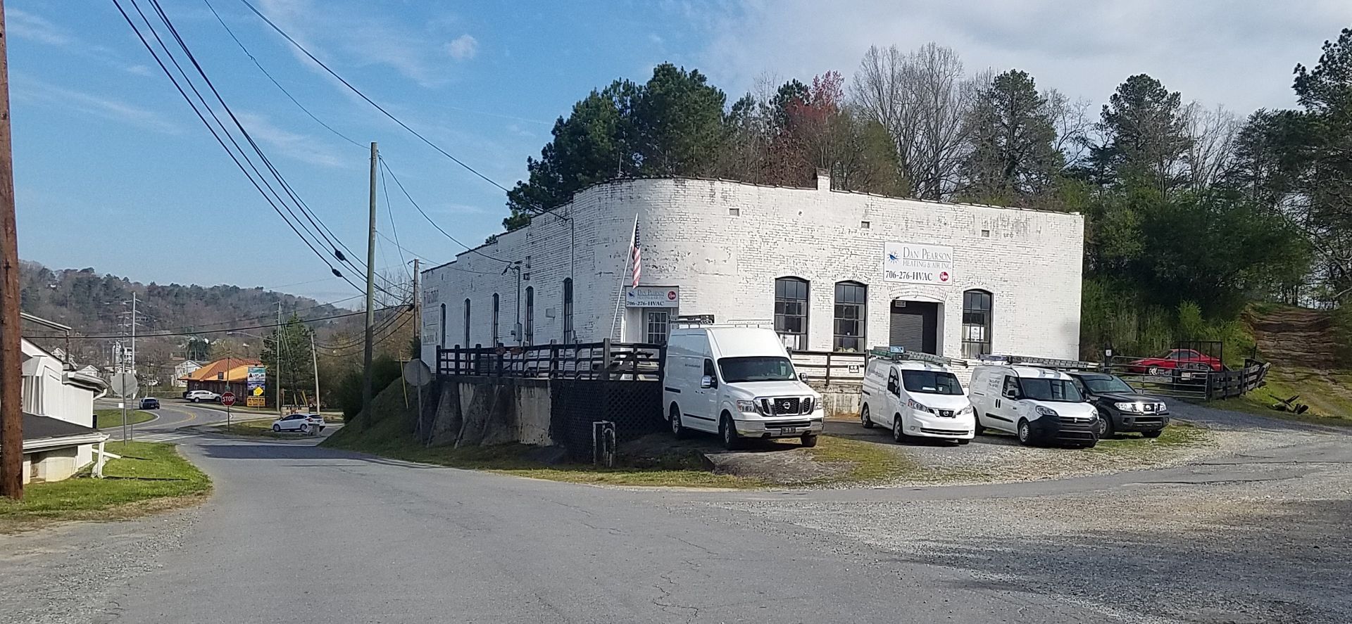 A white building that is the office of Dan Pearson Heating & Air with HVAC trucks parked in front.
