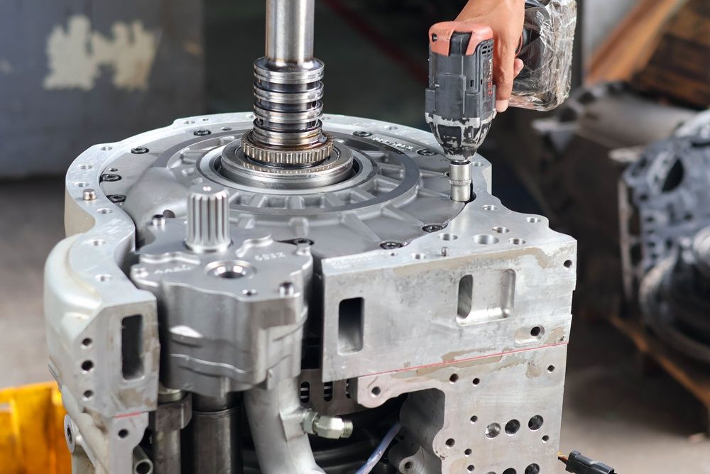 Mechanic using a power tool on a metal gearbox assembly in a workshop