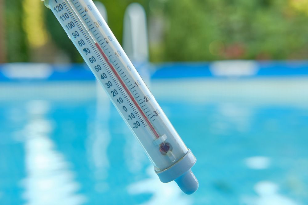 Thermometer measuring pool water temperature; blue water, green background.