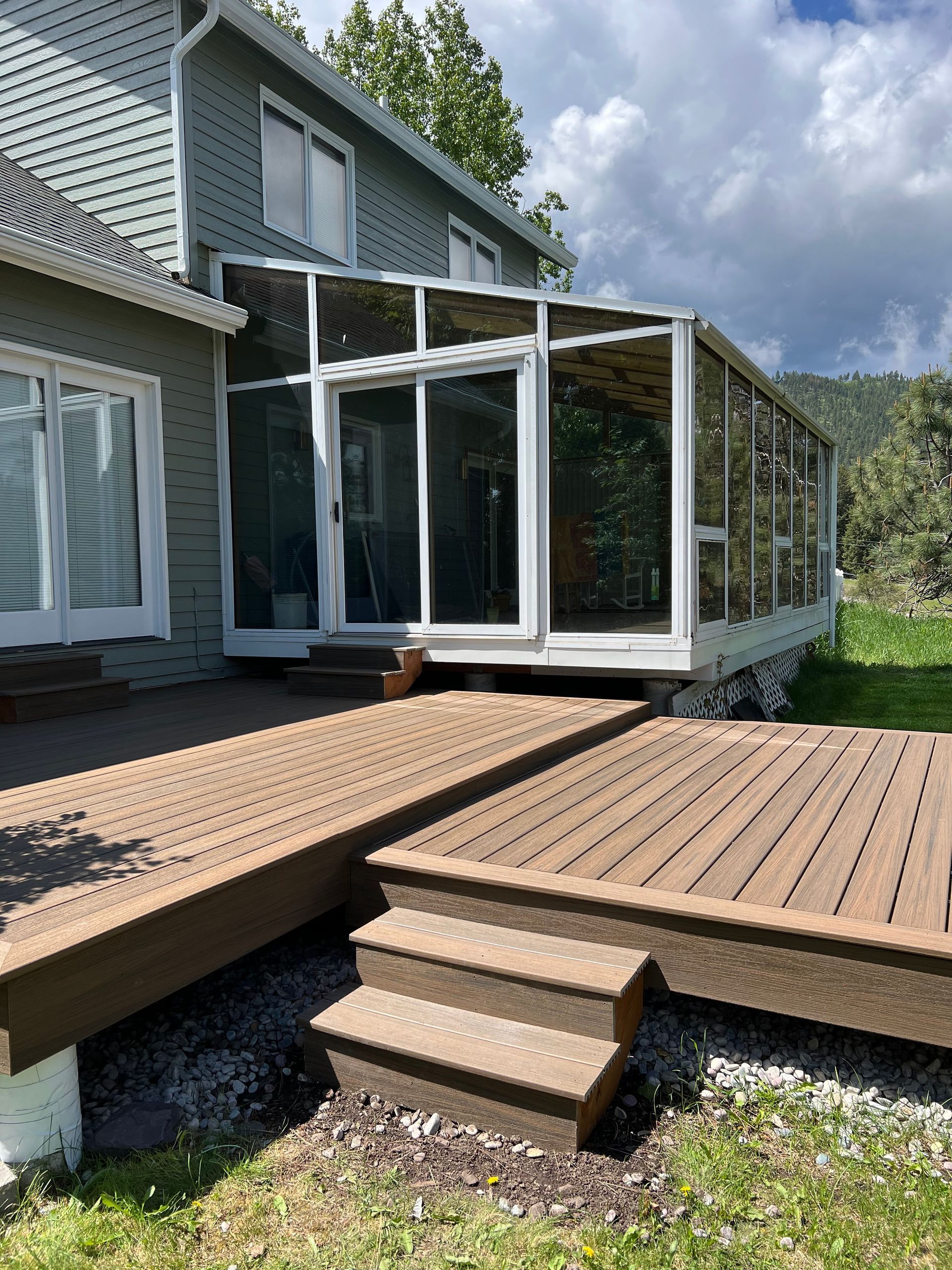 Backyard deck with steps leading to a sunroom attached to a house.
