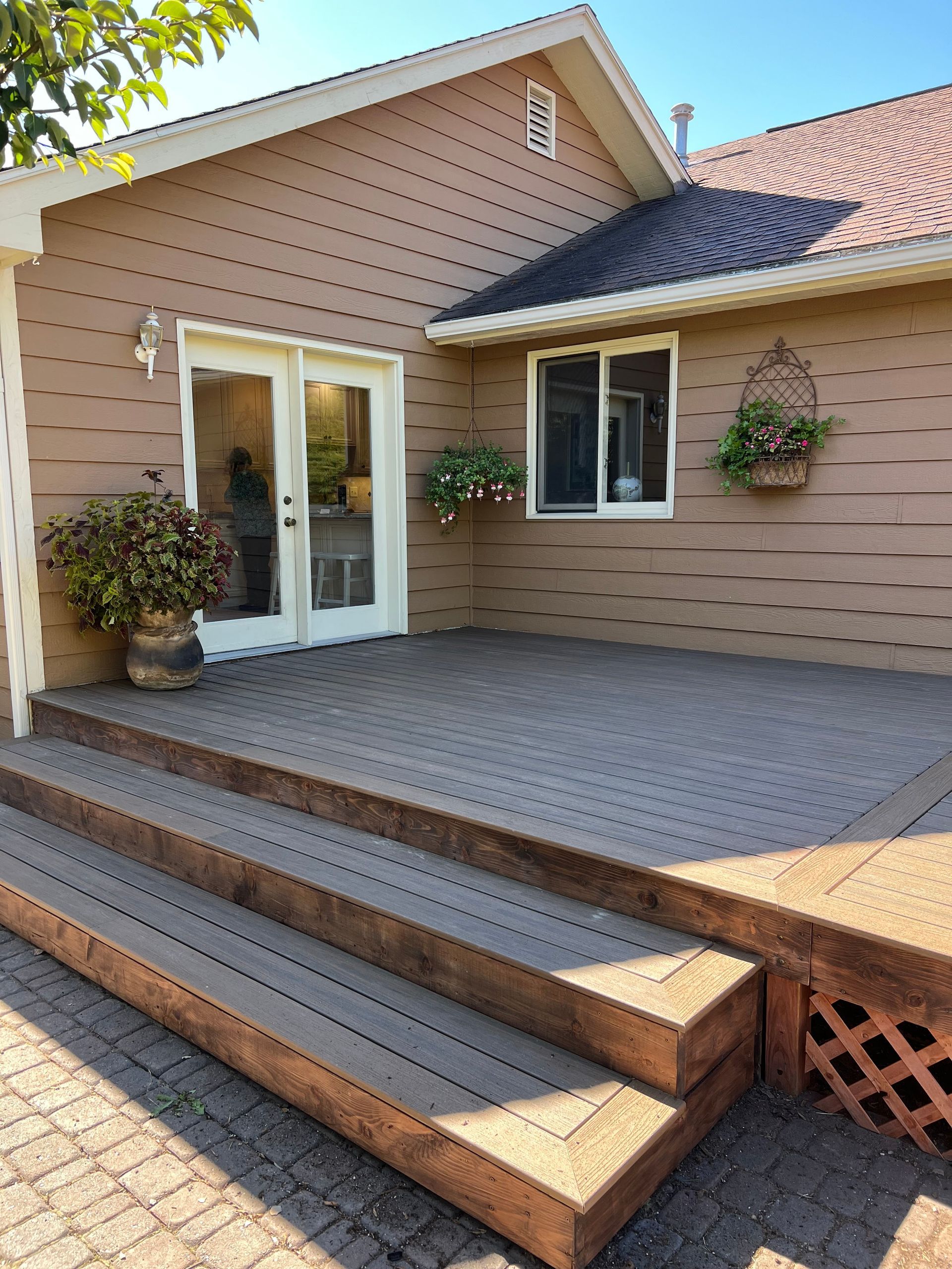 Brown house exterior with deck and steps. French doors, window, and hanging flower baskets.