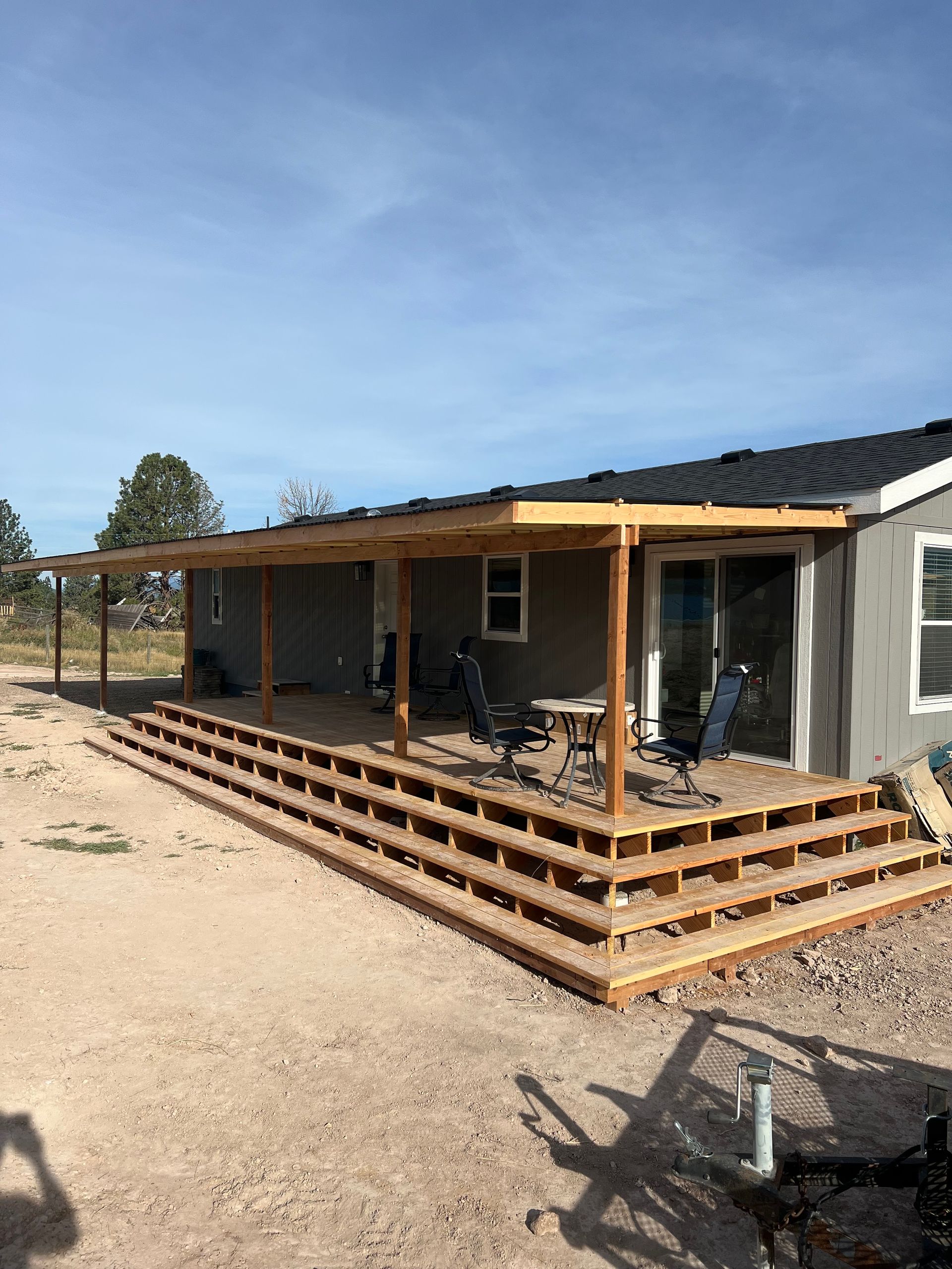 Wooden deck with steps and covered patio attached to a gray house, on a sunny day.