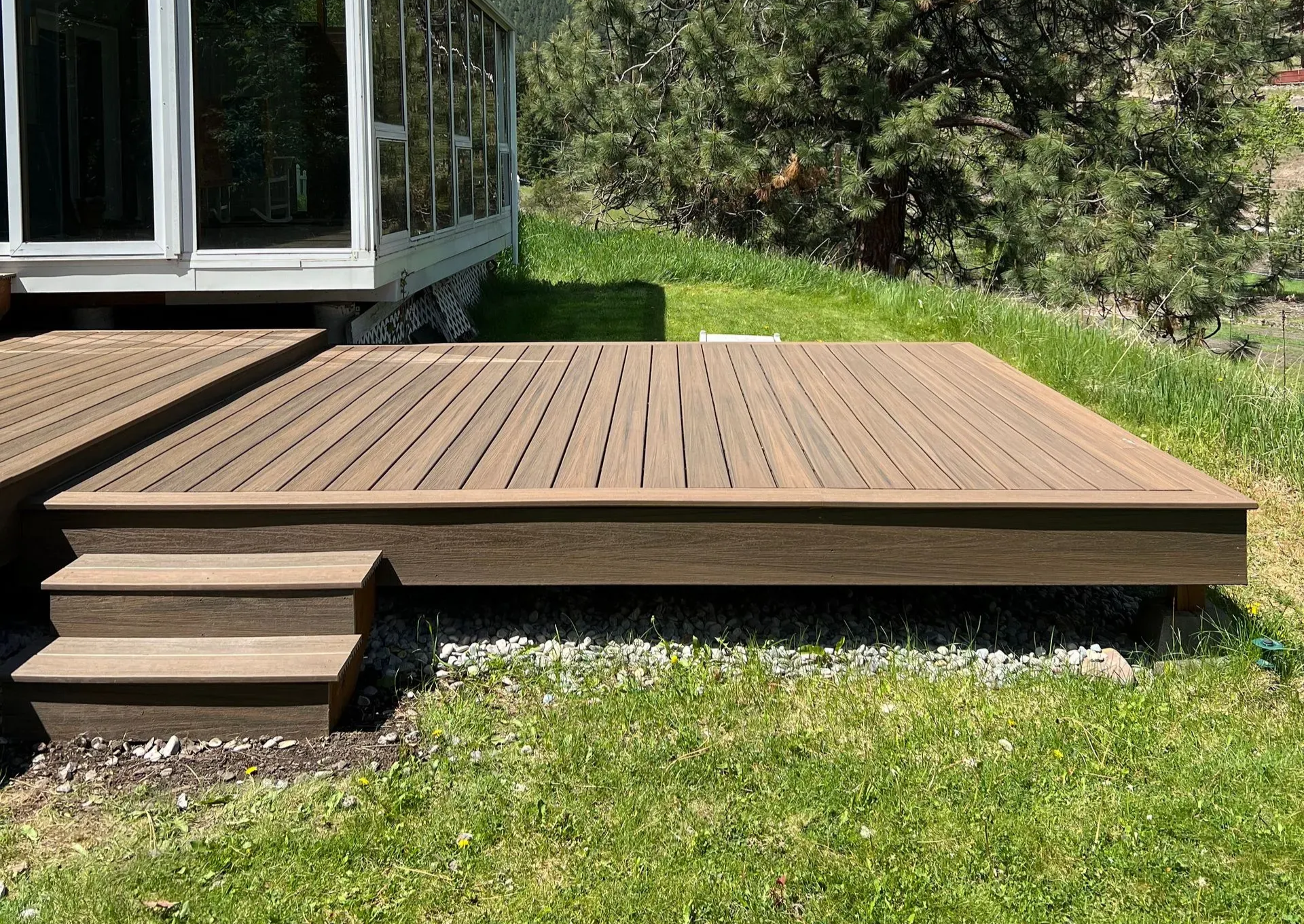 Wooden deck with glass railing overlooks a city and fall foliage.