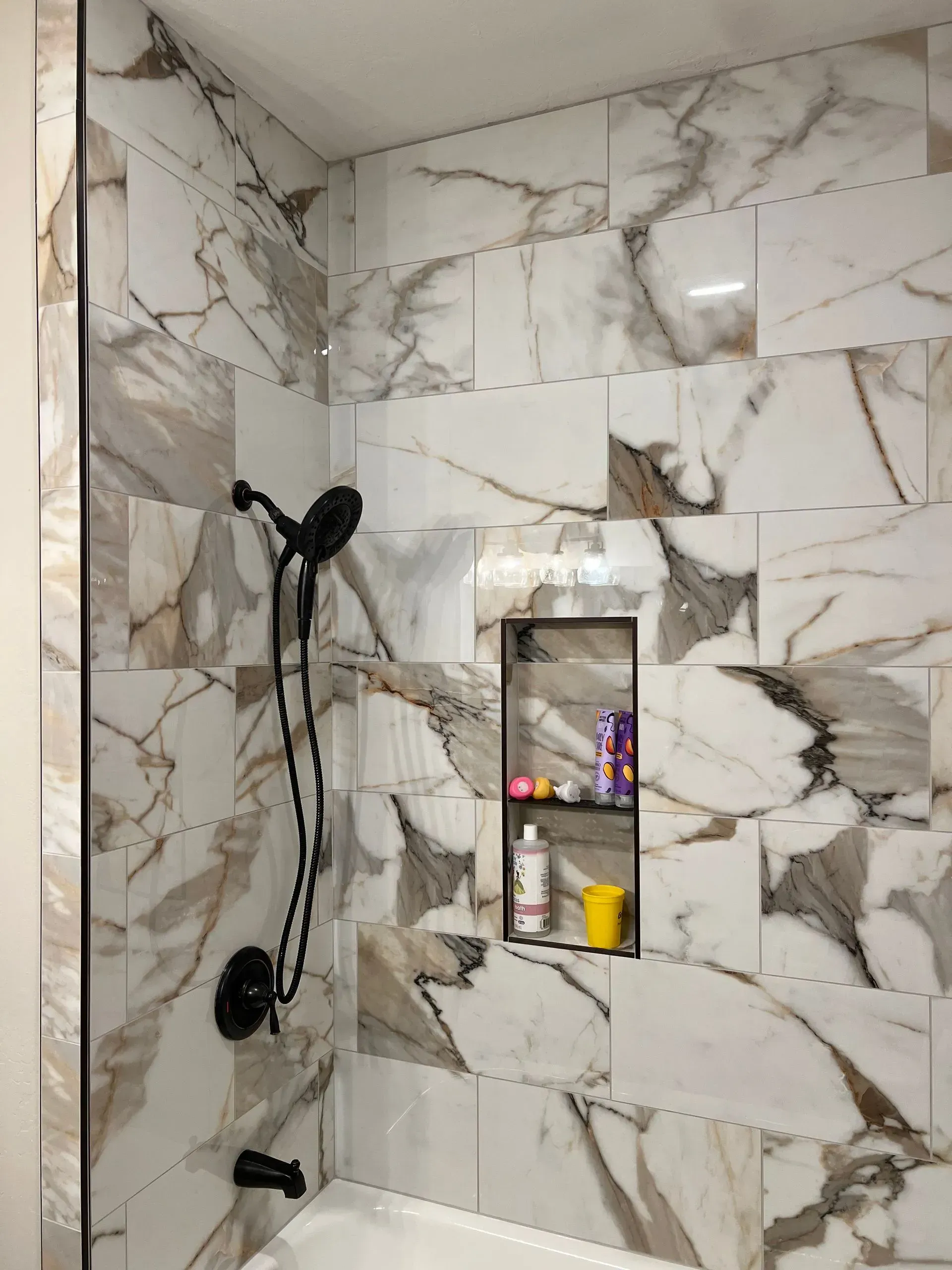 Modern shower with glass doors, white subway tile walls, dark floor, and chrome fixtures.