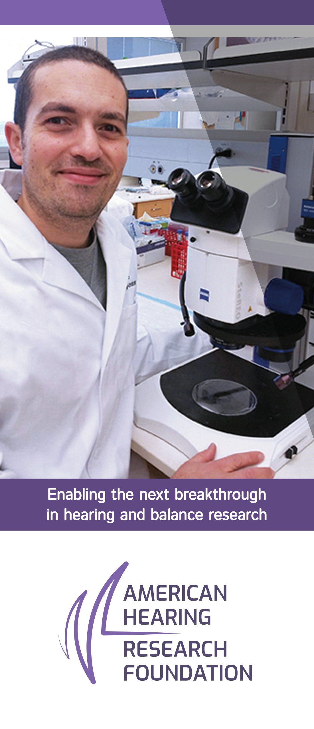A man in a lab coat is standing in front of a microscope.