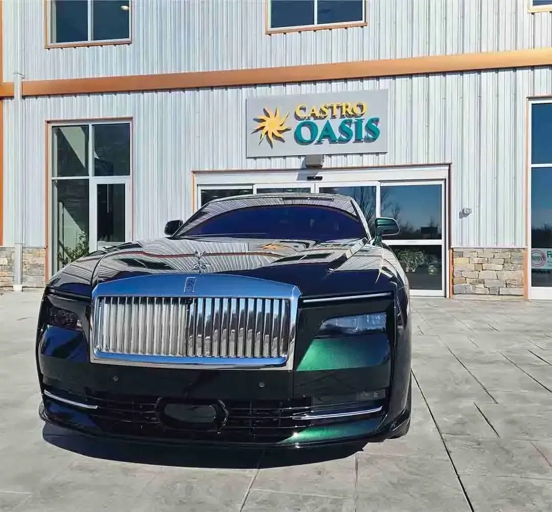 A dark green Rolls-Royce parked in front of a building with a sign that reads 