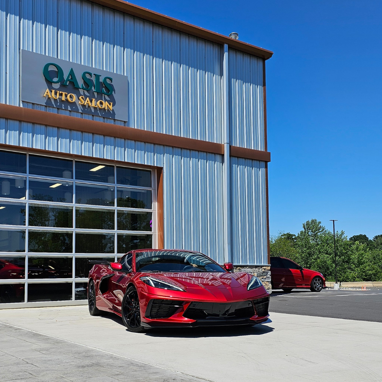 A shiny red sports car parked in front of the Oasis Auto Salon building under a clear blue sky.