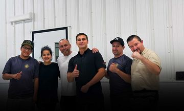 A group of six people stand in a line against a white wall, smiling and posing for a group photo.