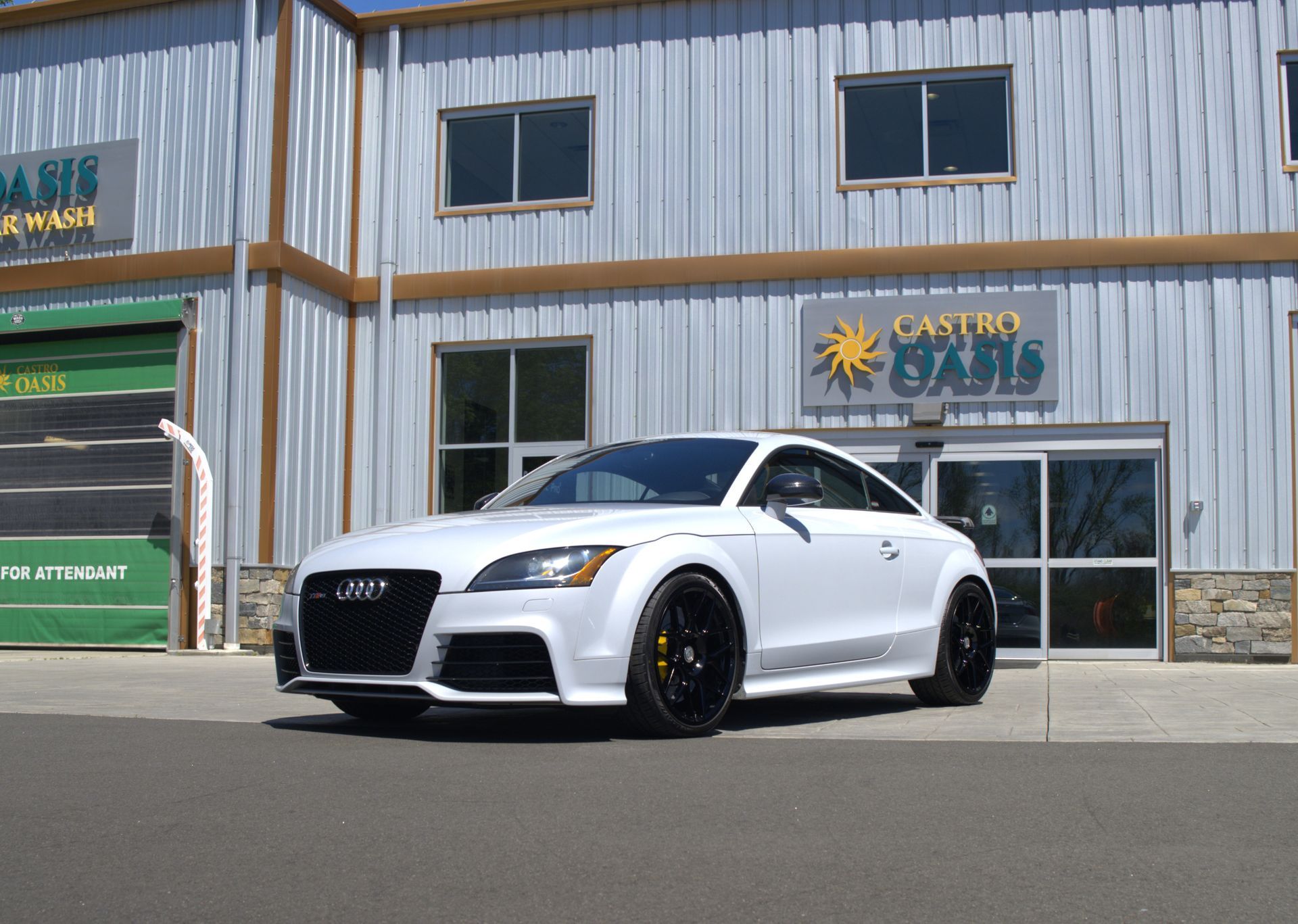 A white Audi TT sports car with black rims parked in front of a business building named Castro Cars.