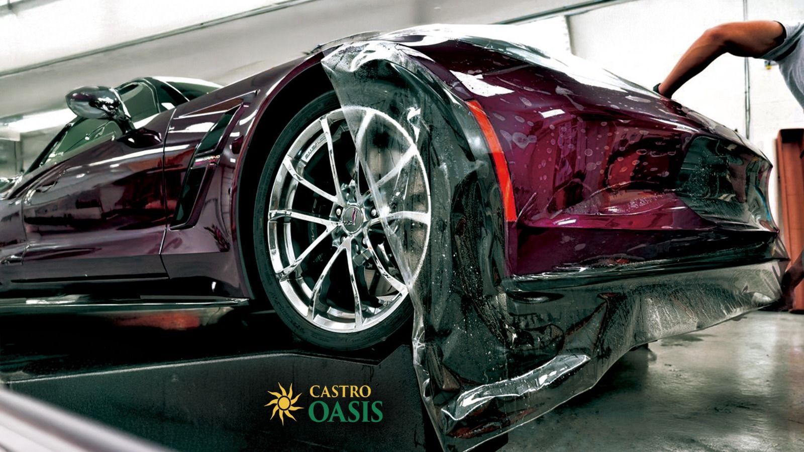 A person applies protective film to the front bumper of a dark purple sports car in a garage.