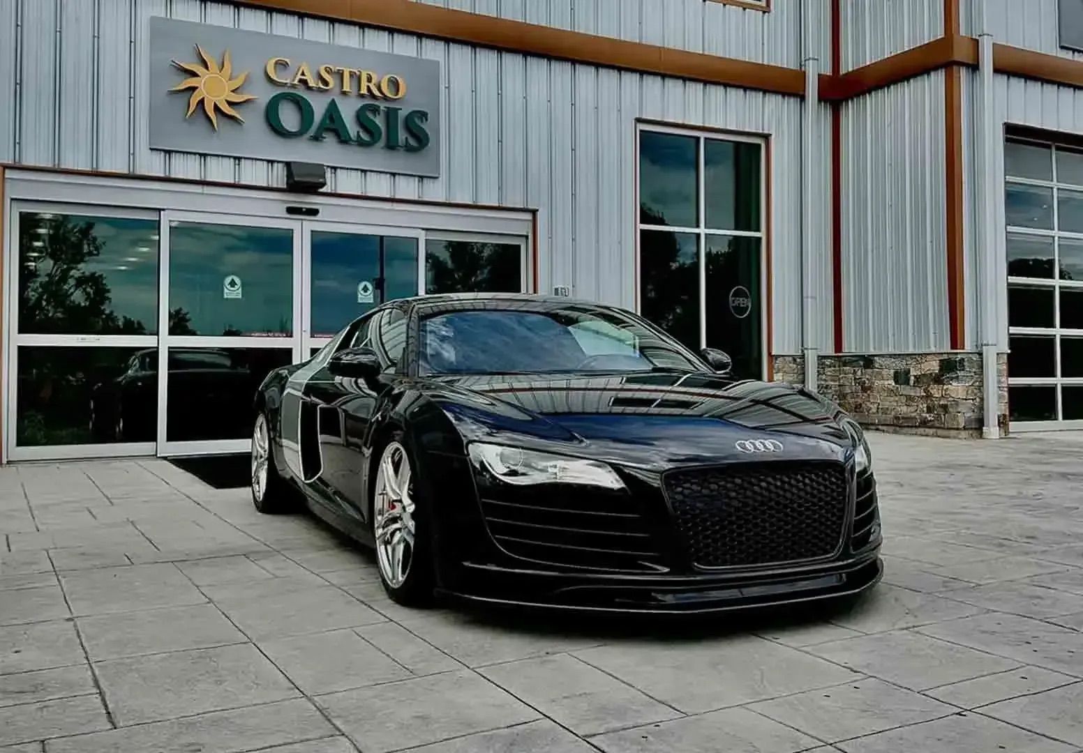 A black Audi R8 parked on a paved lot in front of a building with a 