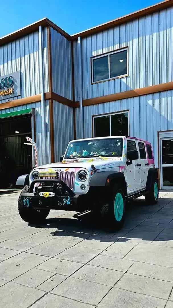 A white Jeep with teal wheels and colorful, hand-drawn graffiti parked in front of a metal-sided building.