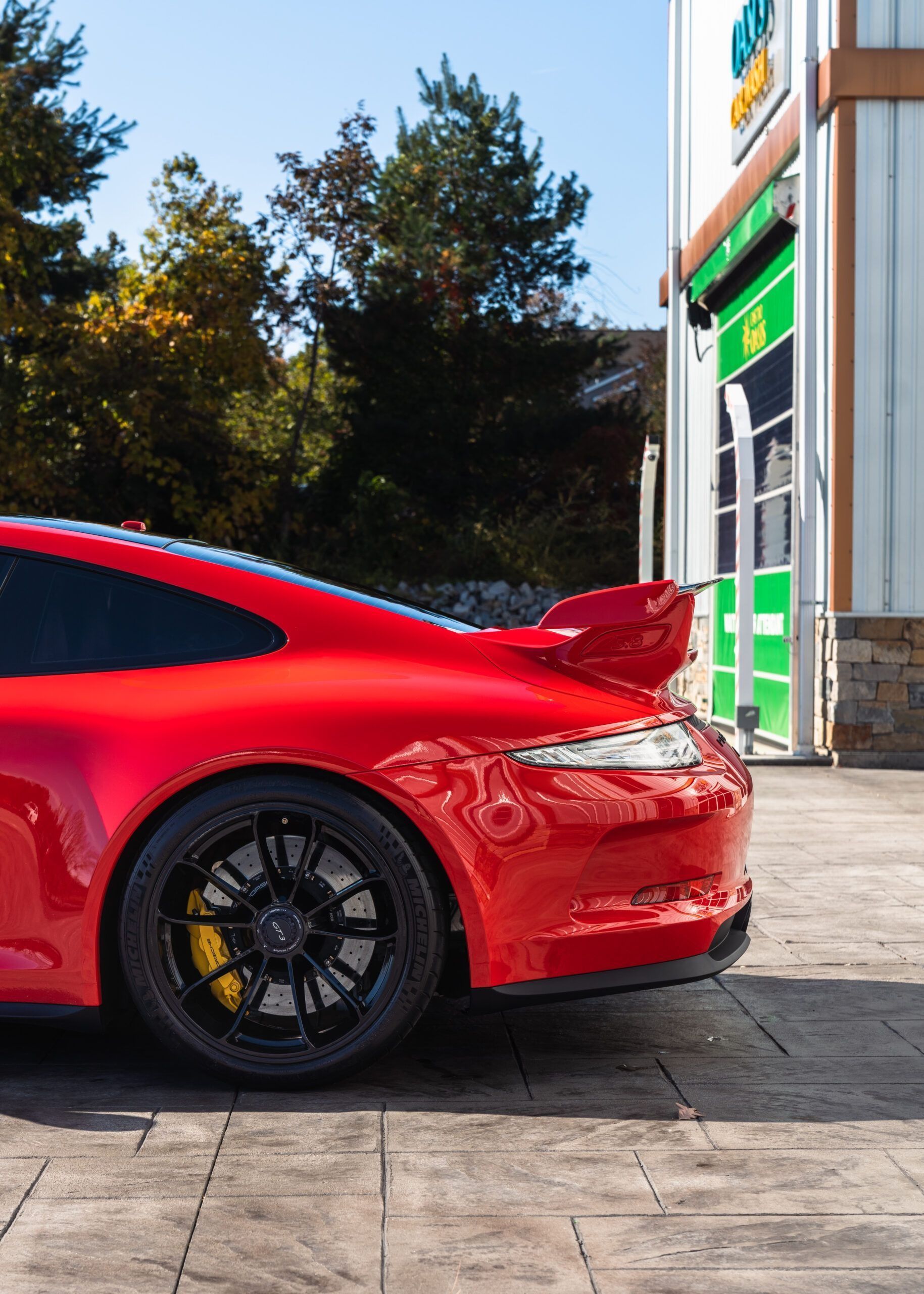 A bright red Porsche 911 sports car parked on a stone driveway in front of a building.