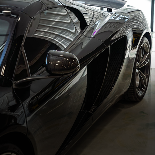 A sleek, glossy black McLaren sports car, showcasing its side profile, side mirror, and air intake vent.