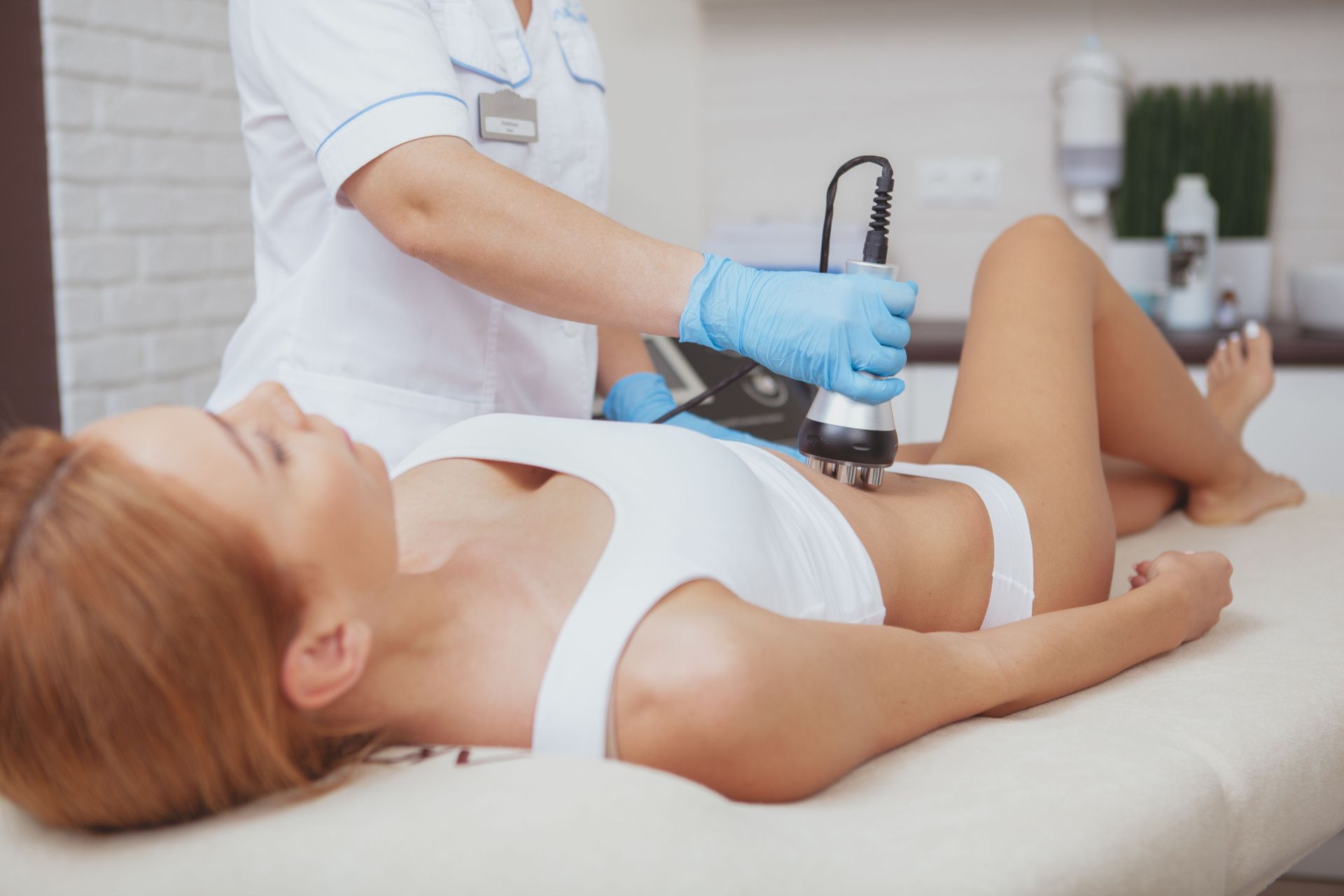 a woman is laying on a bed getting a cavitation treatment on her stomach .