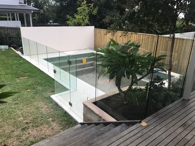 A swimming pool is surrounded by a glass fence and a wooden deck.