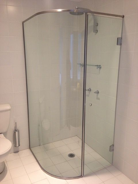 A bathroom with a curved glass shower door and a toilet.