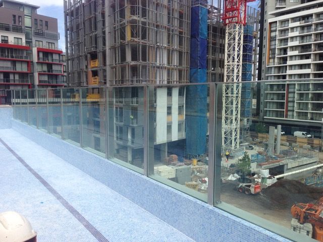 A swimming pool with a glass railing and a view of a building under construction.