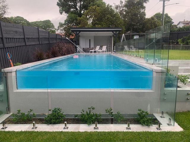 A large swimming pool surrounded by a glass fence in a backyard.