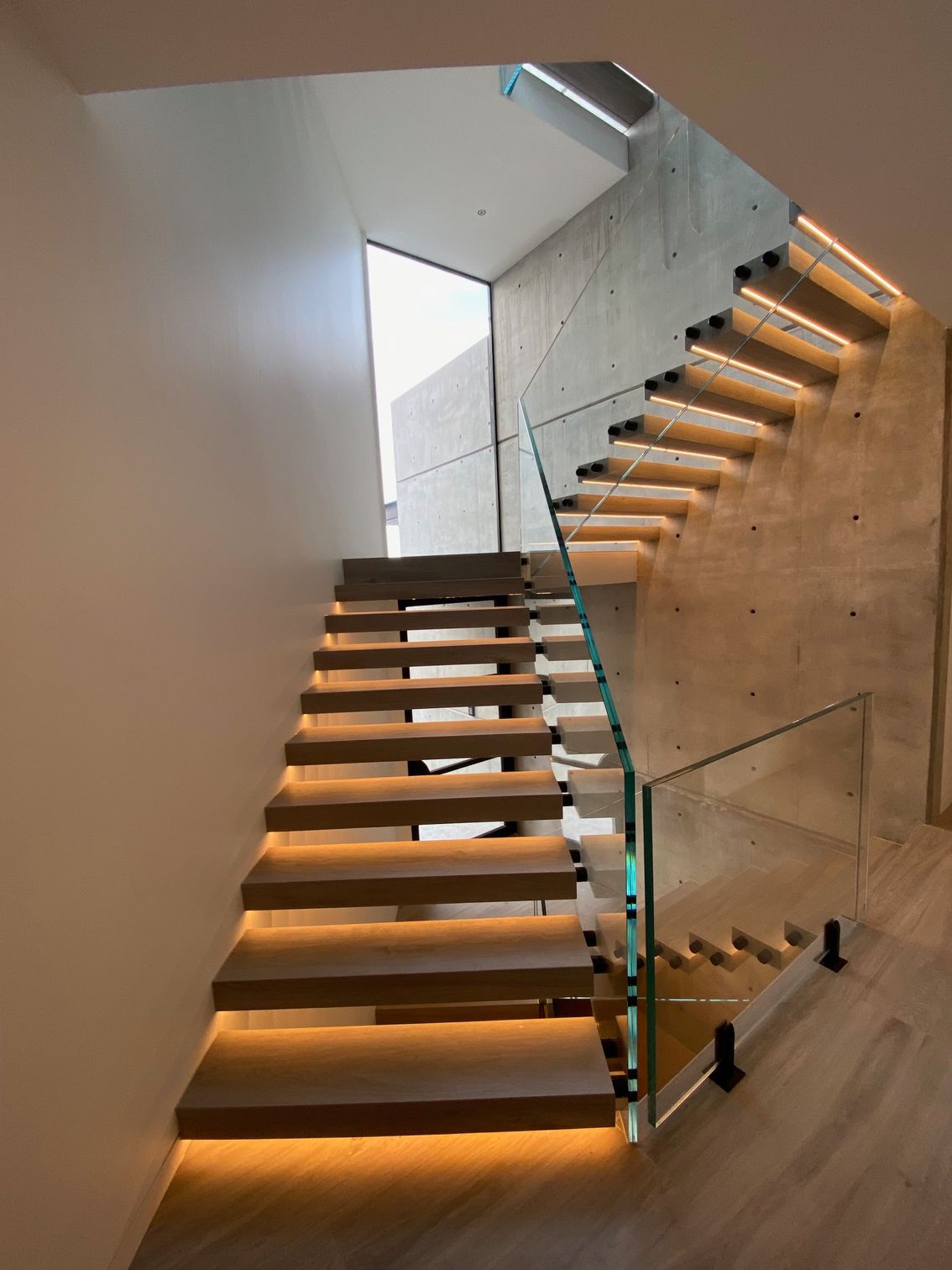 A modern staircase with wooden steps and a glass railing.