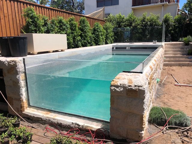 A swimming pool with a clear glass wall is being built in a backyard.