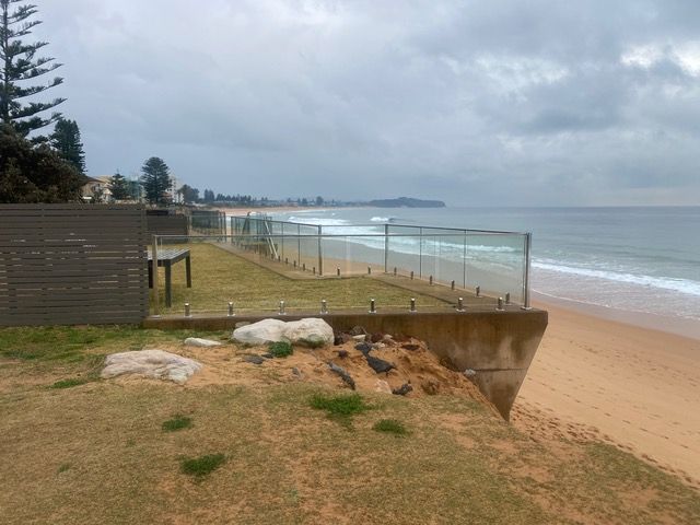 A view of a beach from a cliff with a glass fence.