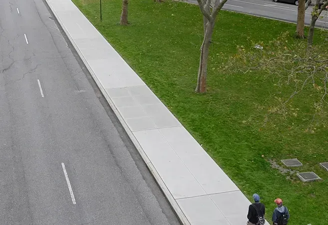 Two people are walking down a sidewalk next to a road.