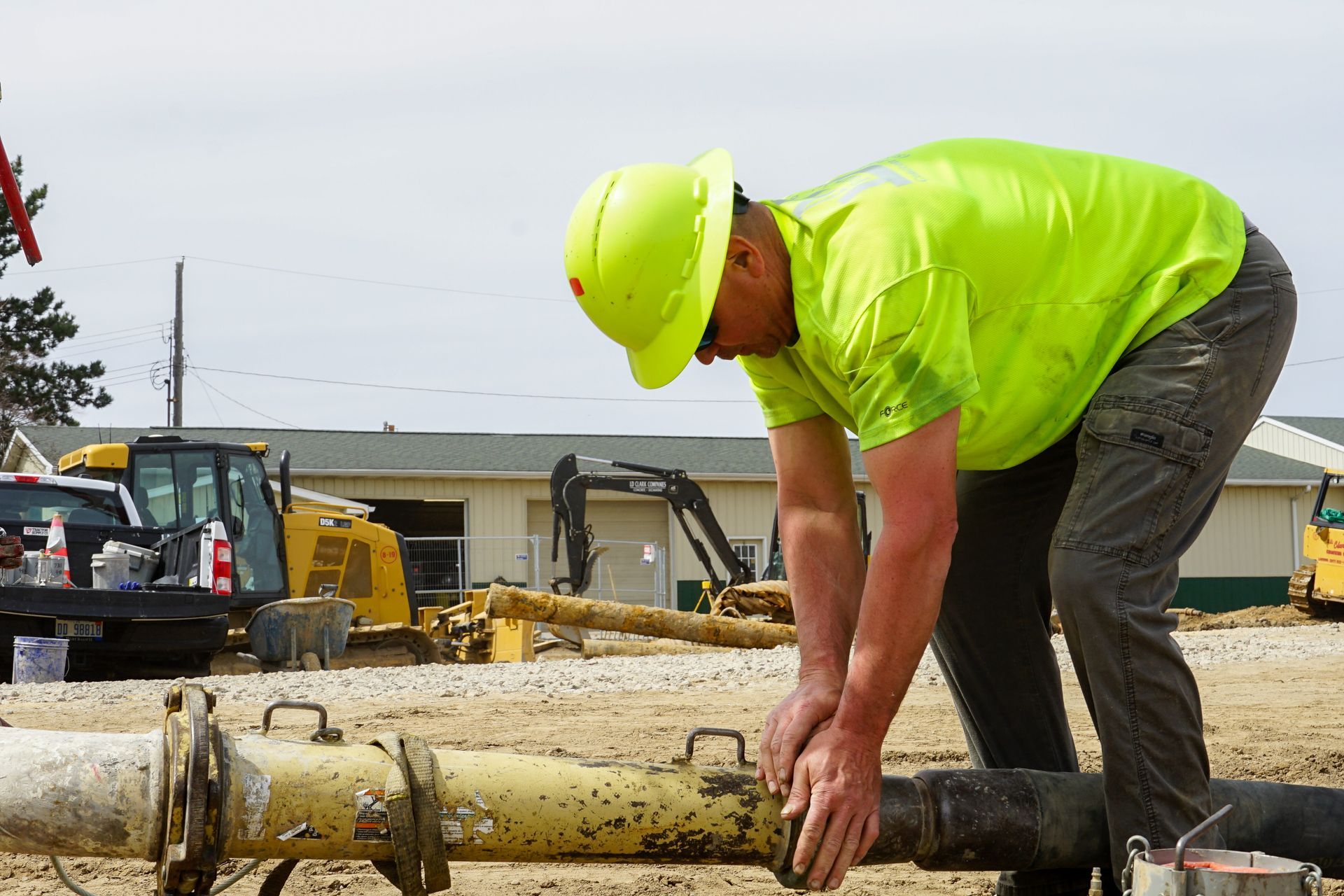 A man wearing a hard hat and a neon yellow shirt is working on a pipe.
