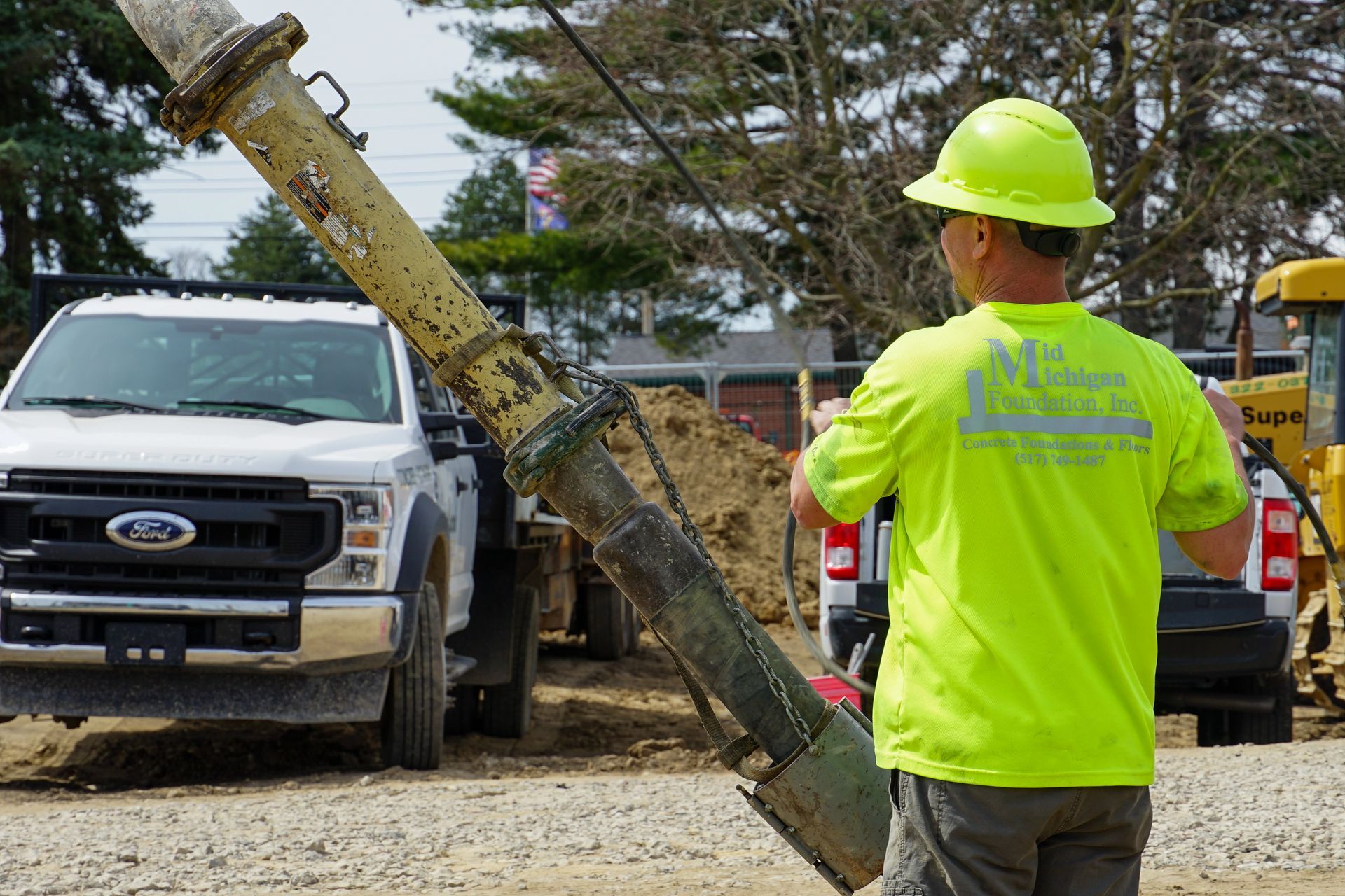 A man wearing a yellow hard hat is standing in front of a truck.