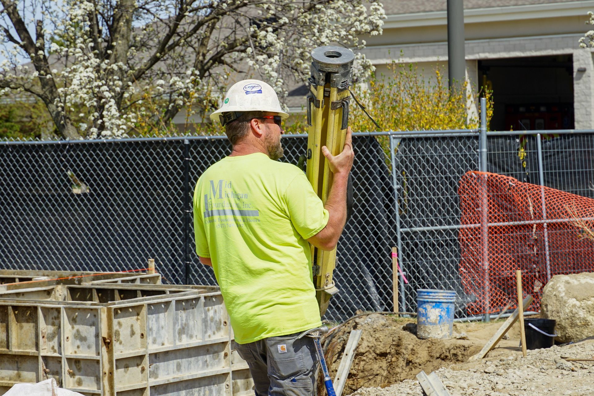A construction worker is standing on a construction site holding a pole.
