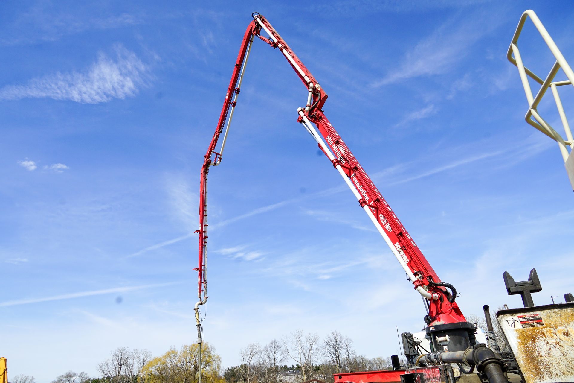A red concrete pump is being used to pour concrete on a construction site.