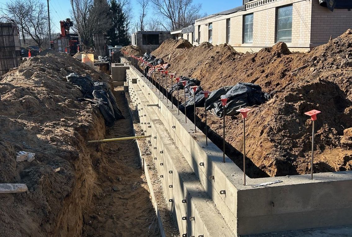 A concrete wall is being built in a trench next to a house.