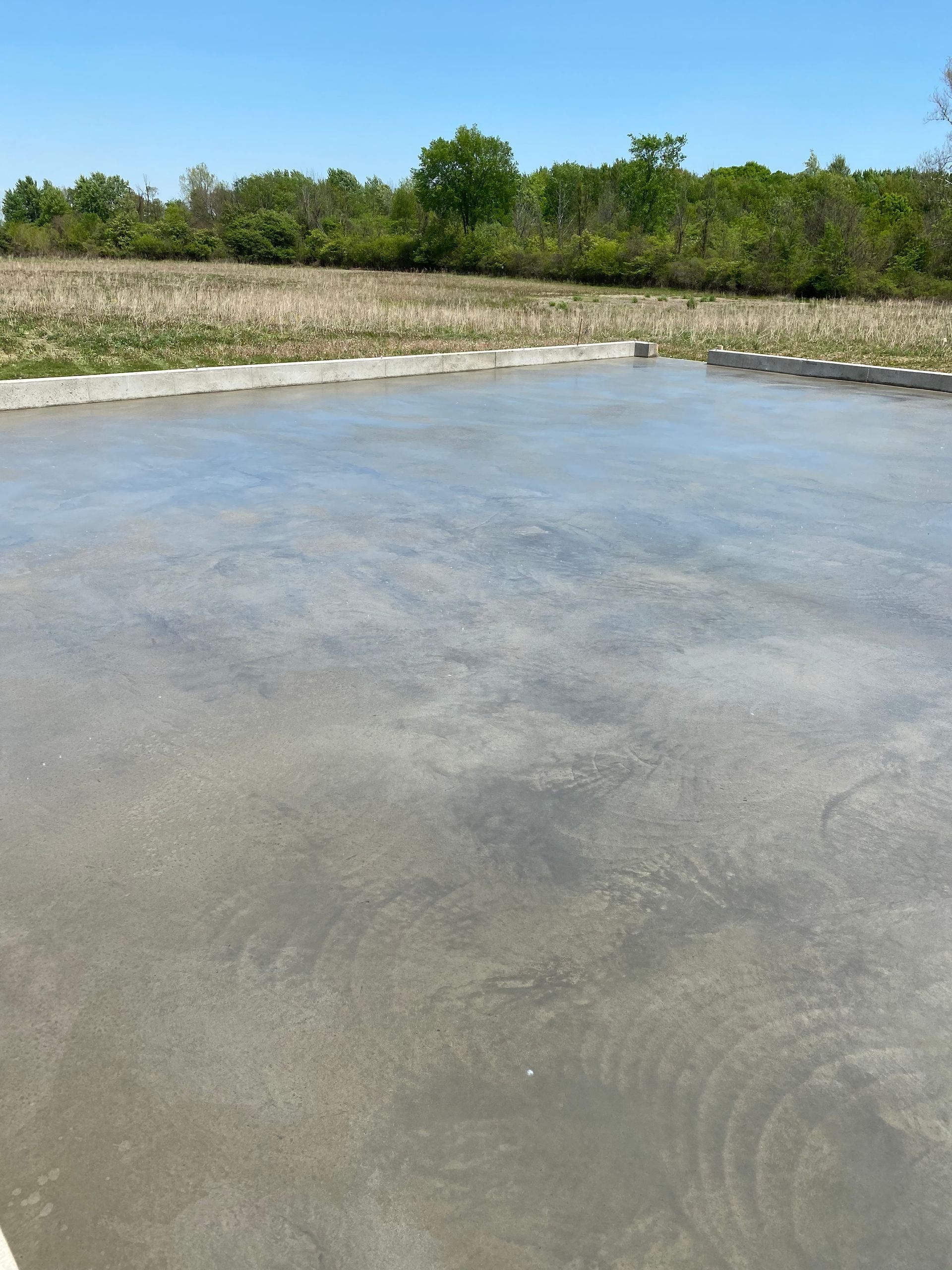 A concrete driveway is being built in a field with trees in the background.
