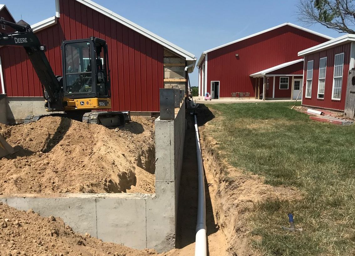 A bulldozer is digging a trench in front of a red barn.