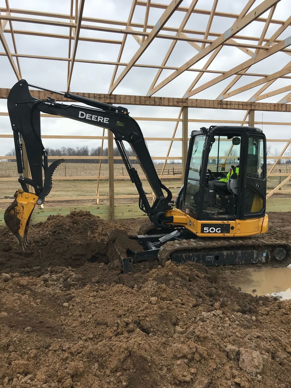 A small excavator is digging a hole in the dirt in a barn.